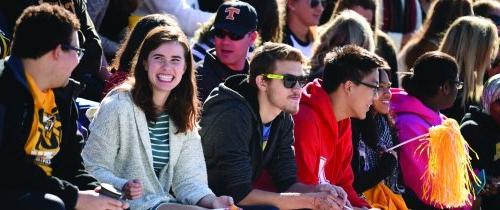 Students smiling sitting on bleachers in football stadium